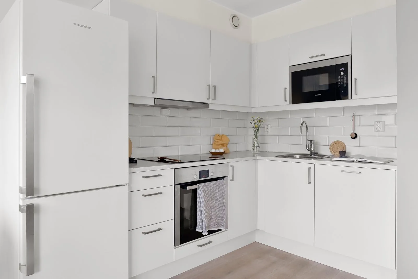 Cozinha nível económico: cozinha pequena em L, frentes brancas com puxadores, azulejo metro, frigorífico solto e forno simples em inox