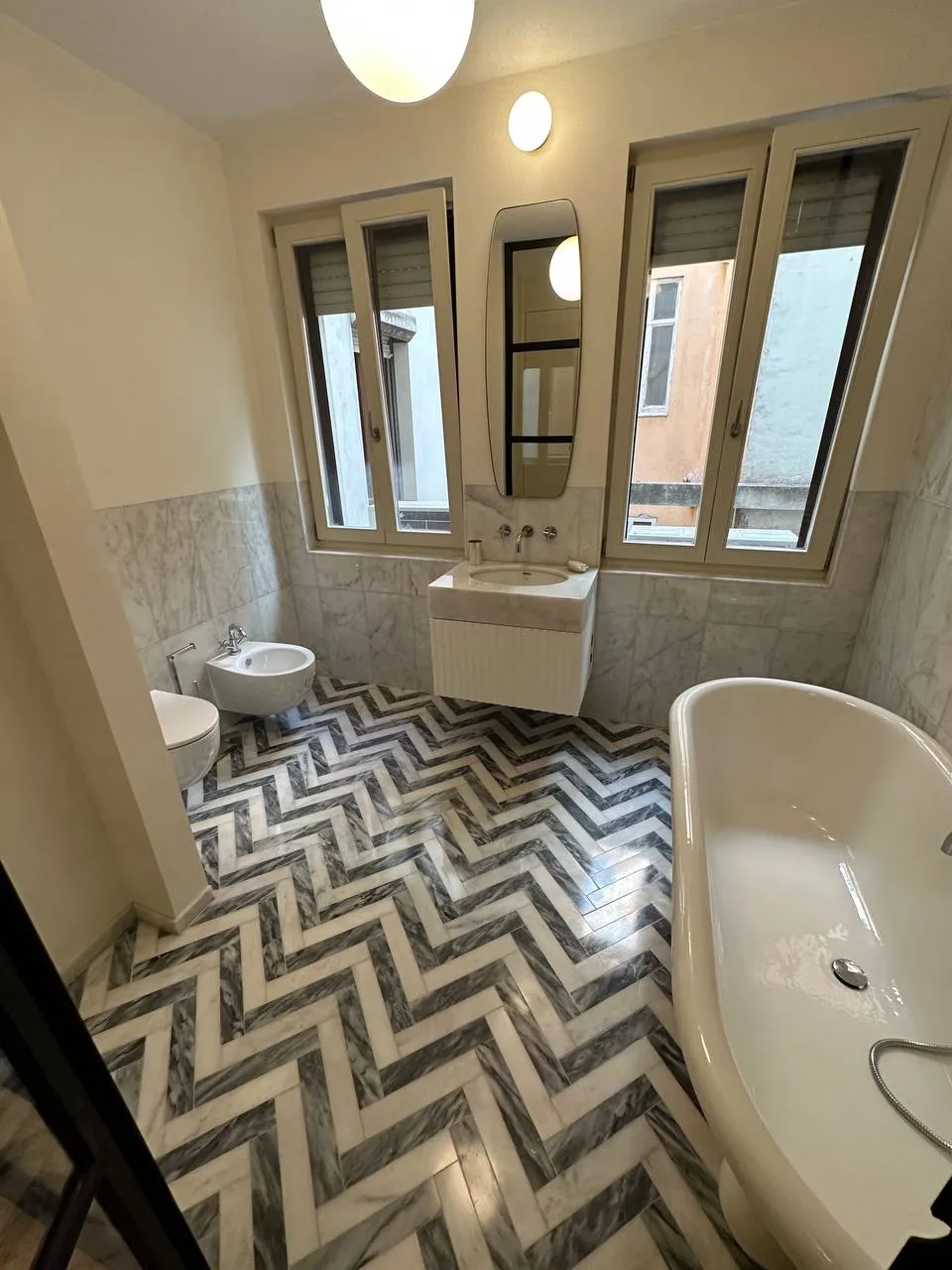 Casa de banho vista da porta: banheira junto às janelas, bidé e chão em mármore ao espinha