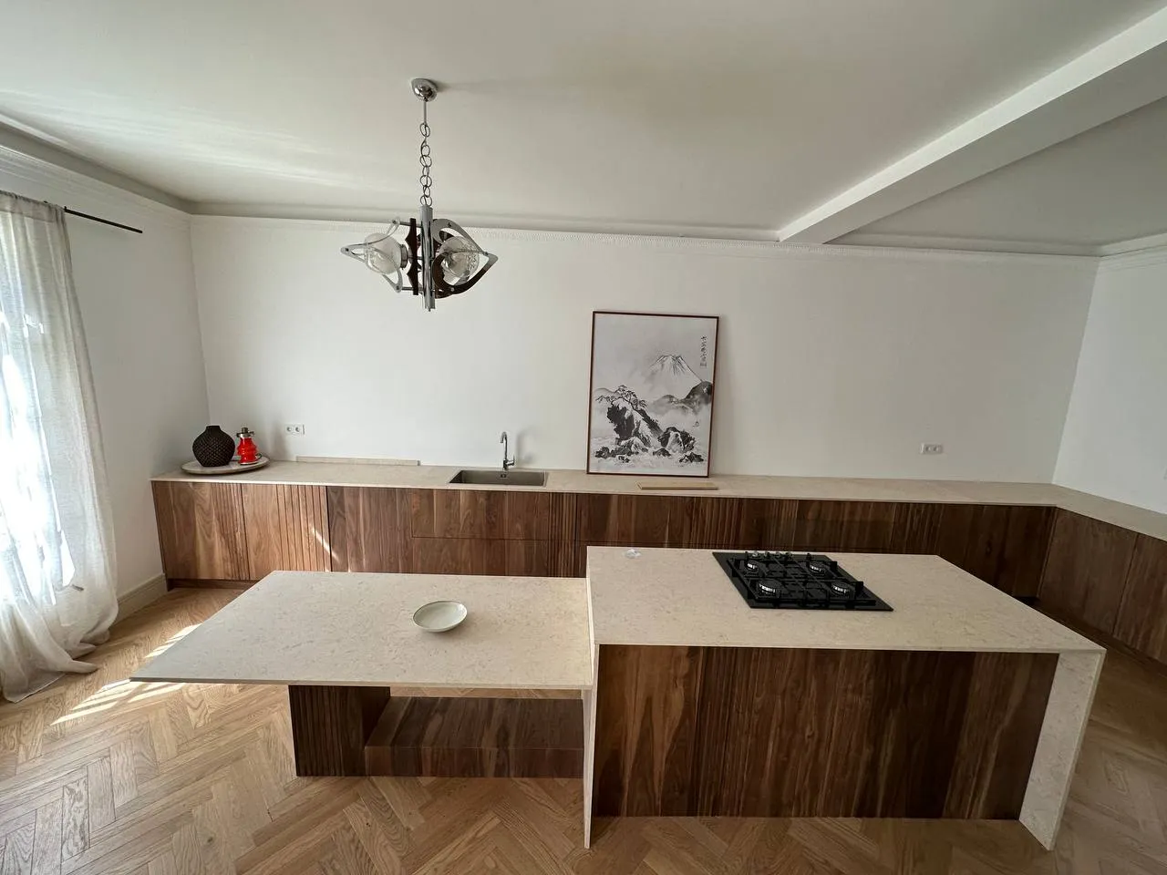 Cozinha com armários em nogueira, ilha em pedra clara com placa integrada e parquet em espinha