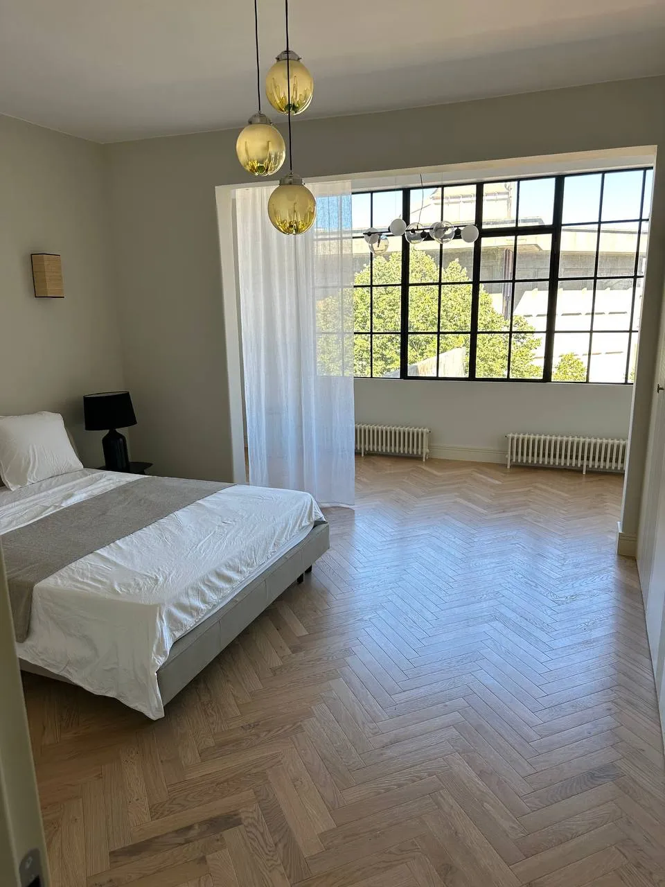 Quarto com cama arrumada, parquet em espinha e janela de perfil preto até ao teto