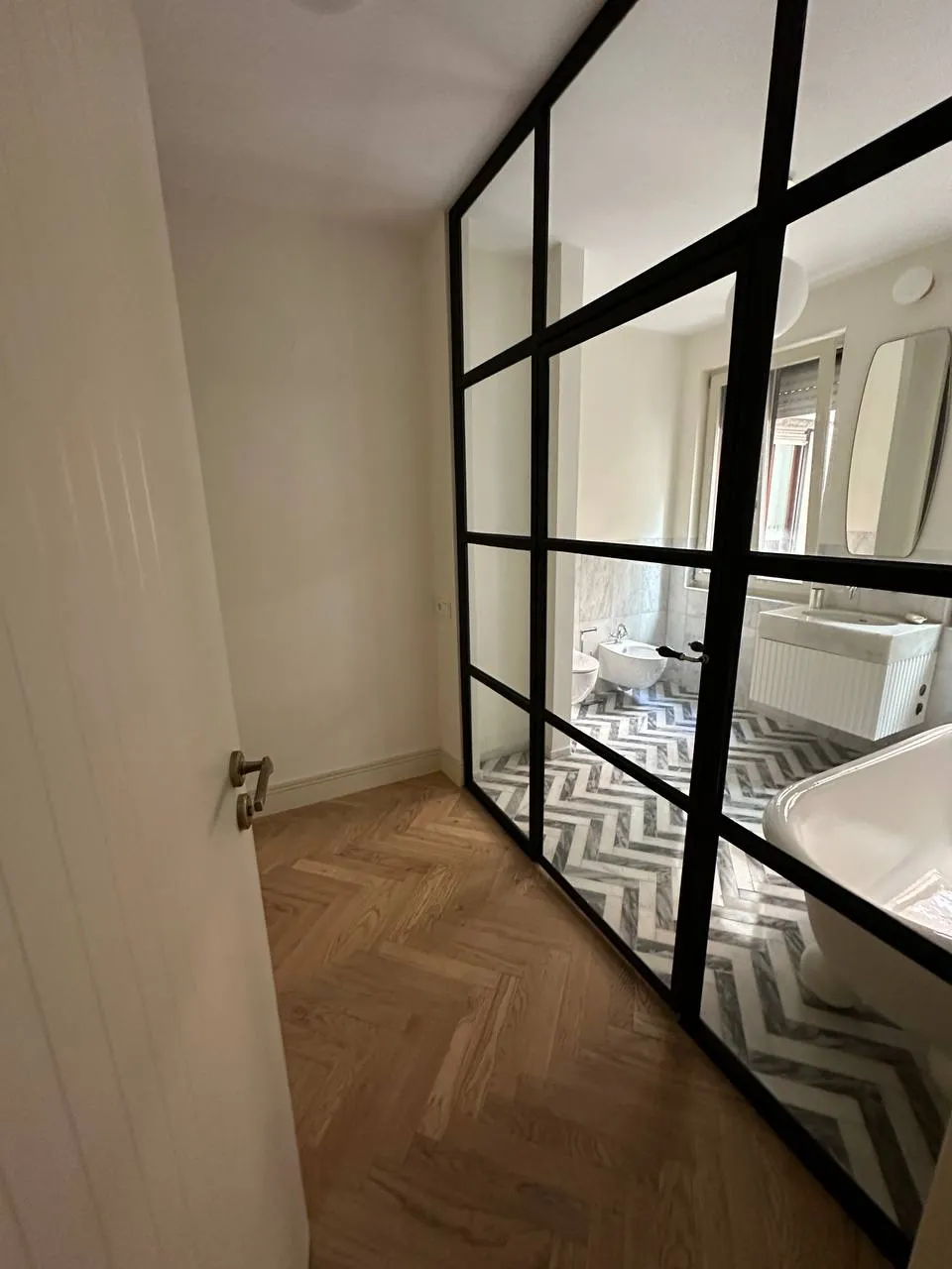 Roupeiro com portas espelhadas de perfil preto, refletindo a casa de banho em mármore