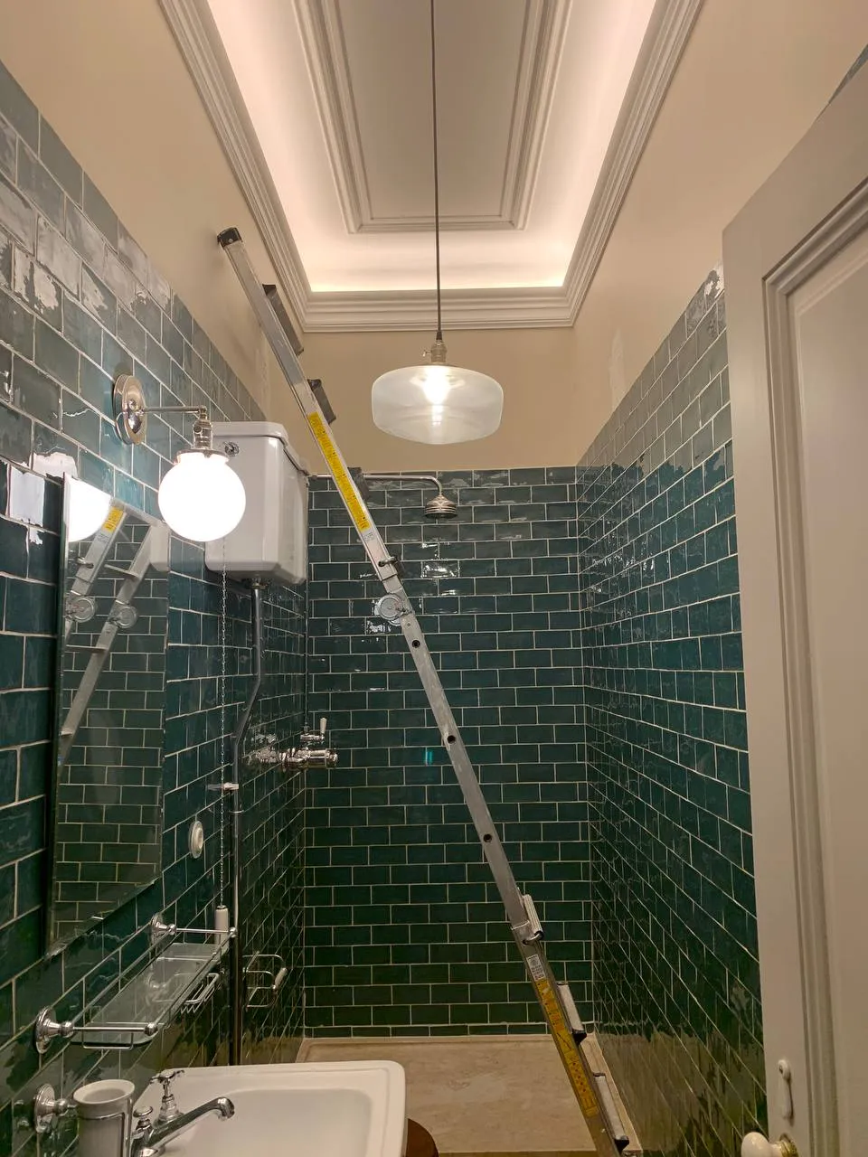 Segunda casa de banho na reta final: azulejo metro verde, sanca com iluminação indireta, candeeiro suspenso em vidro e escadote ainda no duche