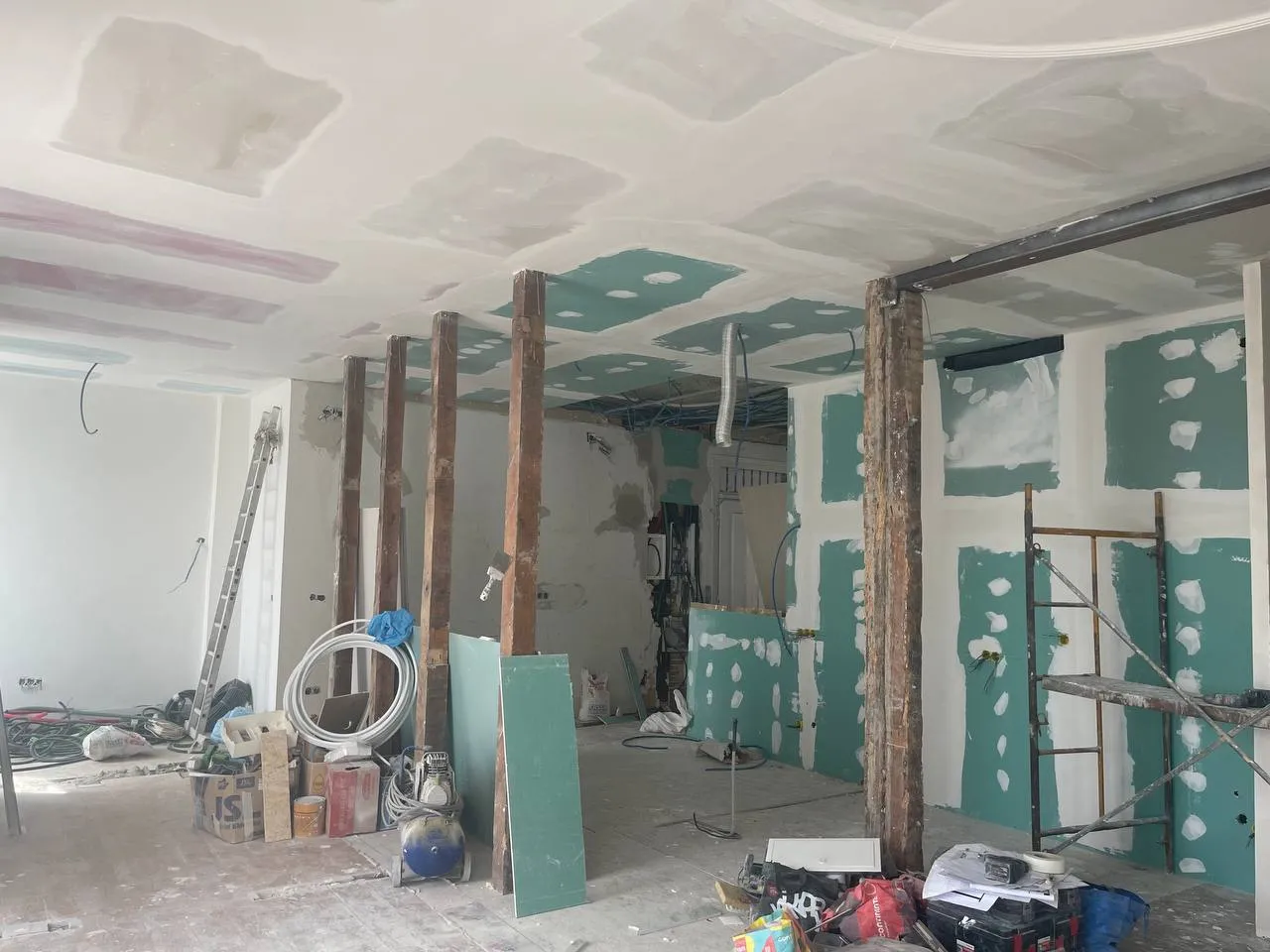 Apartamento em obra: gesso cartonado aberto, vigas de madeira expostas e andaimes