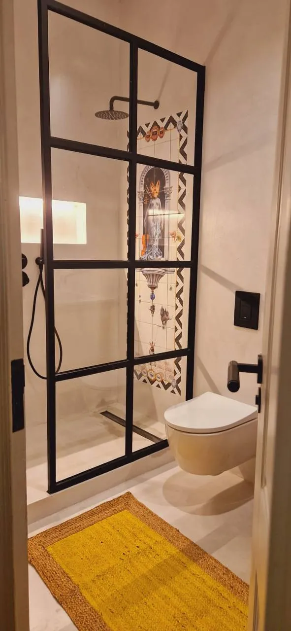 Casa de banho com duche de vidro quadriculado preto e tapete amarelo